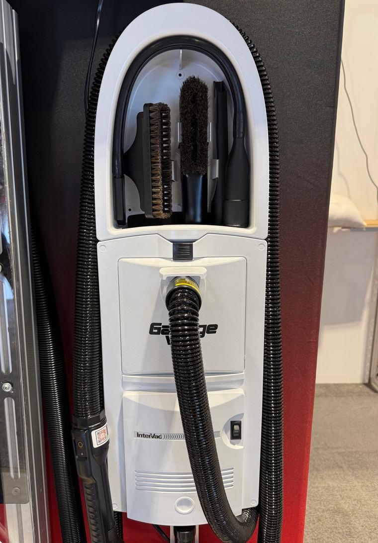 A white GarageVac GH120 mounted on a wall, tools stored in the top caddy and the stretch hose connected at the inlet.